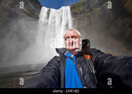 metà 40s grigio capelli single maschio turista prende selfie imbarazzante a skogafoss cascata islanda Foto Stock