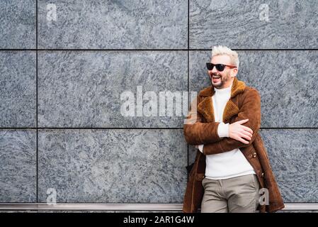 L'uomo allegro si levano in piedi con le sue braccia piegate e sorride felicemente, l'uomo barbuto con i calici del sole ride Foto Stock