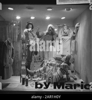 Parrucchiere Mario, titolare del parrucchiere The Trend di Amsterdam, con parrucca Mario e pittore Simon Postuma (con parrucche) mentre si posa in vetrina, insieme a due modelli Data: 5 novembre 1965 luogo: Amsterdam, Noord-Holland Parole Chiave: Modelli fotografici, parrucchieri, pittori, moda, parrucche Nome personale: Postuma, Simon Foto Stock