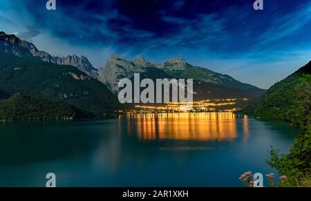 Il bellissimo Molveno di notte con la luce riflessa sul grande lago. Sullo sfondo ci sono grandi montagne Foto Stock