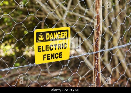 Cartello di pericolo appeso alla recinzione elettrica con gli alberi sullo sfondo Foto Stock