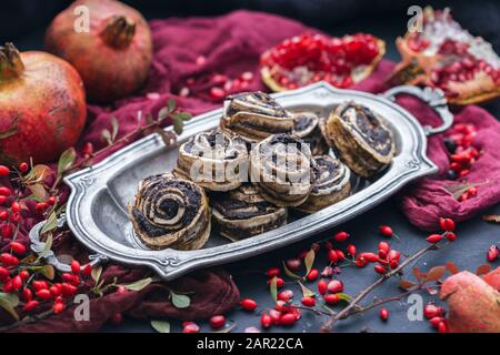 Rotolette grezze di papavero vegano su una piastra di metallo con melograno semi e rosehips in uno sfondo scuro Foto Stock
