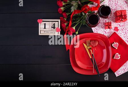 Cena di un giorno in San Valentino con tavolo con regalo, rose rosse, cuori con due wineglasses su sfondo scuro. Vista dall'alto, piatto. Foto Stock