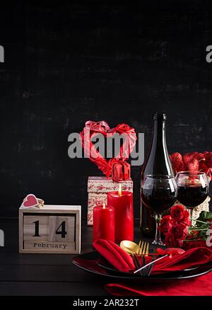 Cena di un giorno in San Valentino con tavolo con regalo, rose rosse, cuori con due wineglasses su sfondo scuro. Foto Stock