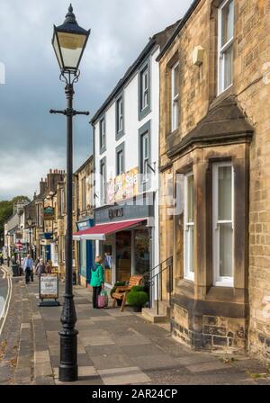 Negozi d'epoca ed edifici con persone, su un lato di Galgate, nella storica città del mercato di Barnard Castle, Teesdale, County Durham, Inghilterra, Regno Unito. Foto Stock