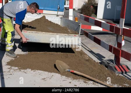 Giovane operaio edile in cantiere chiude il portellone di un rimorchio caricato di sabbia. Giovane operaio edile; uomo; rimorchio; pendente; costr Foto Stock