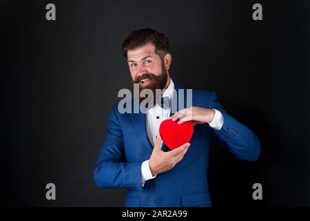 Posso aiutarla. Giornata mondiale del cuore. Brutale hipster barbuto in abito formale. Uomo d'affari in cravatta di prua. Assistenza sanitaria. Decorazione di giorno di San Valentino. Tuxedo uomo con cuore rosso. Festa di festa. Concetto di amore. Foto Stock