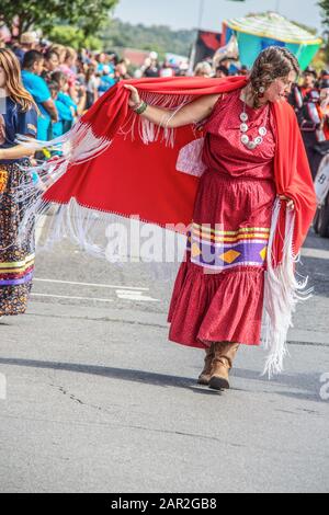 8-31-2019 Tahlequah USA - Native American woman in abito tradizionale e stivali cowboy swirls il suo mantello rosso frangiato mentre cammina a Cherokee National ho Foto Stock