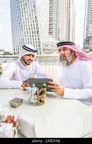 Due uomini d'affari con abiti tradizionali emirates a Dubai - adulti anziani e giovani che hanno affari negli Emirati Arabi Uniti Foto Stock