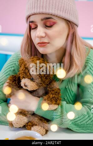 Ritratto di una bella ragazza in maglione verde. Bella giovane donna abbracciando Teddy bear. Luci bokeh di fondo Foto Stock