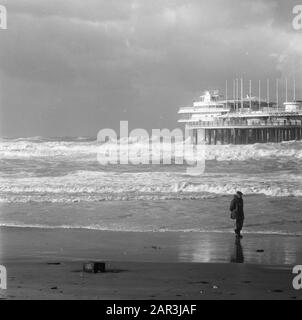 Woerful mare al molo di Scheveningen UN camminatore passeggiate lungo la spiaggia, sullo sfondo il surf Annotazione: Il 13 novembre 1973 una tempesta pesante infuriato, che ha causato un sacco di danni nelle foreste Veluwe. Venti di 135 km all'ora sono misurati a Groningen Data: 13 novembre 1973 Località: Scheveningen [l'Aia], Zuid-Holland Parole Chiave: Moli, tempeste, spiagge, mari Foto Stock
