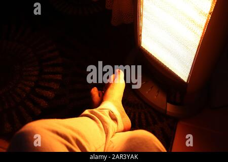 Scatto ad angolo alto di una persona che si stende i piedi dentro di fronte a un riscaldatore in una stanza Foto Stock