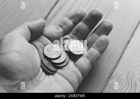 Scala di grigi ad alto angolo di una persona che ne tiene in mano monete su superficie di legno Foto Stock