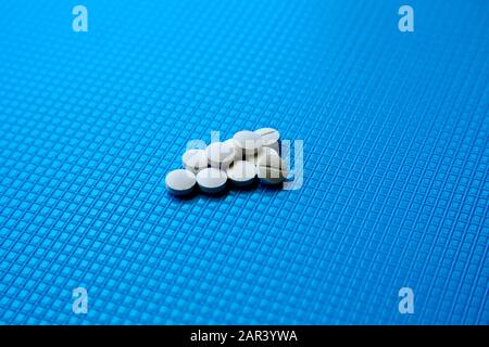 Un colpo ad alto angolo di un mazzo di pillole bianche sopra una superficie blu Foto Stock