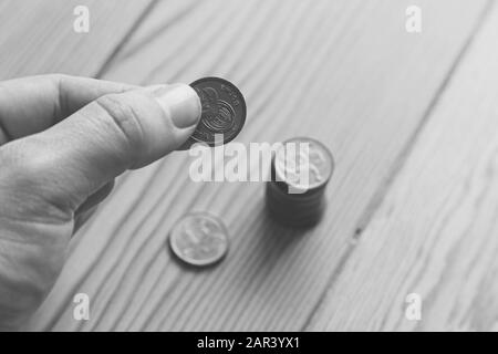 Scala di grigi ad alto angolo di una persona che tiene un moneta su una superficie di legno Foto Stock