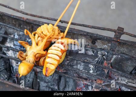 Spiedino di calamari con bastoni grigliati su una stufa a carbone. Calamari grigliati su una stufa a carbone. Foto Stock