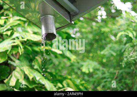 L'acqua piovana scorre lungo le grondaie e scende verso le grondaie di pioggia dal tetto. Foto Stock