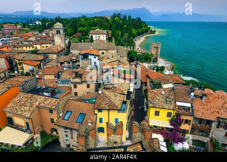 Splendida vista sui tetti antichi e sulle strade turistiche della località di Sirmione dal castello Scaliger. Bellissimo lago di Garda con montagne sullo sfondo, L Foto Stock