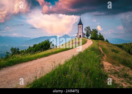 Tramonto paesaggio con chiesa carina sulla collina. Paesaggio alpino e fantastica affascinante chiesa di San Primoz con montagne sullo sfondo al tramonto, Jam Foto Stock