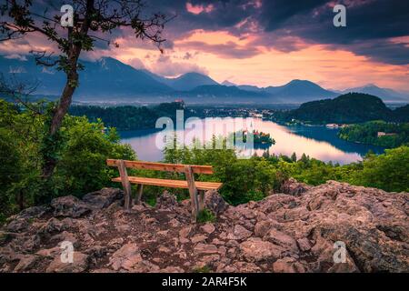 Pittoresco luogo di riposo con panca di legno sulla cima della montagna. Vista panoramica sul lago di Bled e piccola isola al tramonto, Slovenia, Europa Foto Stock