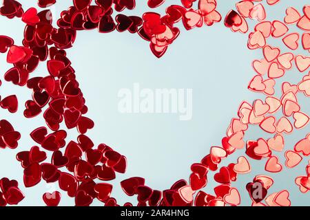 I confetti in lamina rossa sono disposti in una cornice a forma di cuore su sfondo blu. Foto Stock