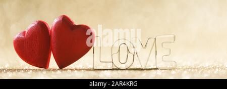 Due rossi in legno fatti a mano il cuore e la parola amore su golden luminose luci glitter sfondo bokeh di fondo Foto Stock