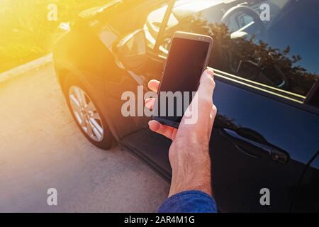Uomo che tiene lo smartphone vicino all'auto. Foto Stock