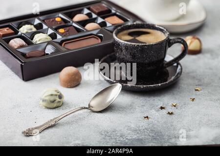 Selezione di caramelle al cioccolato con una tazza di caffè nero e cucchiaio d'argento su sfondo chiaro. Foto Stock