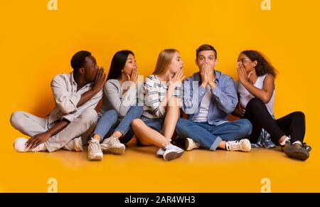 Gruppo di studenti che gossisting su sfondo giallo Foto Stock