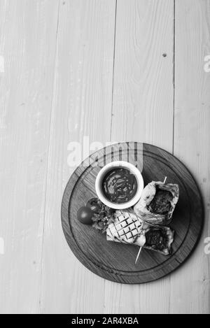 Concetto di portata principale. Carne macinata avvolta con pane di lavasina su fondo giallo di legno. Flatbread con ripieno di maiale o pollo e salsa di peperoncino rosso. Burrito o tortilla serviti in ristorante o caffetteria. Foto Stock