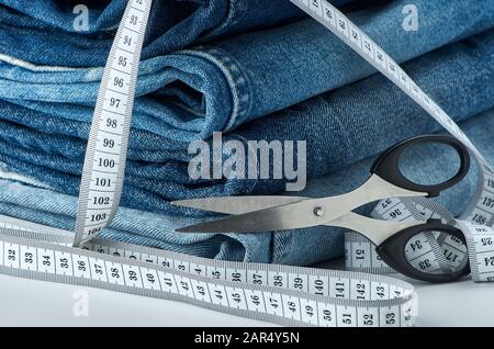 Jeans di cotone blu piegati su un tavolo con un metro a nastro e forbici su uno sfondo bianco isolato. Foto Stock