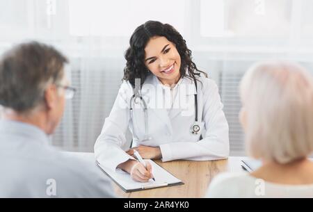 Medico messicano che scrive diagnosi consulenza coppia in ufficio Foto Stock