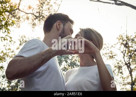 Giovani amanti baciare stand pronti a unire le mani per formare un cuore nel parco. Le coppie adolescenti si amano nel parco. Concetto di giovane coppia Foto Stock