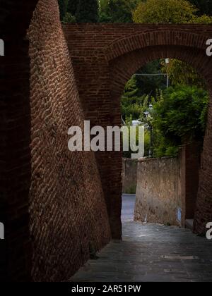 Uno stretto passaggio tra due pareti di mattoni rossi in una vecchia città medievale italiana con una splendida vista Foto Stock