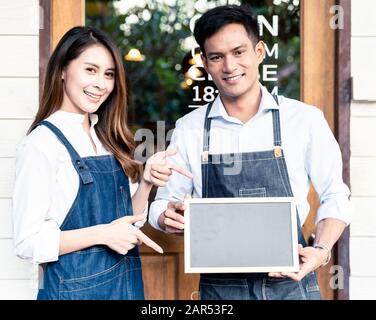 I giovani adulti asiatici proprietari di Small Business Cafe che tengono una lavagna bianca davanti al coffee shop. Utilizzo come concetto PMI di avvio. Raccolto quadrato Foto Stock