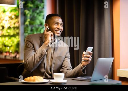 Giovane uomo d'affari africano che parla in cuffie al caffè Foto Stock