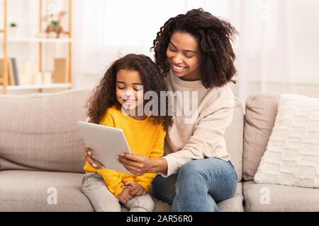 Madre E Figlia Che Utilizzano Il Tablet Watching Cartoons Seduto Sul Lettino Foto Stock