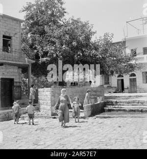 Israele - Peki'nel villaggio di Peki'in Galilea. Una strada freelance alla fonte locale. Ragazzi e uomini hanno guardato l'ombra di un albero. Donne e ragazze fetch acqua Data: 1 gennaio 1963 Località: Israele, Peki'in Parole Chiave: Alberi, villaggi, bambini, pareti, immagini di strada, fonti d'acqua Foto Stock