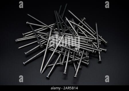 Molti chiodi in ferro da costruzione, parti industriali, isolati su sfondo nero Foto Stock