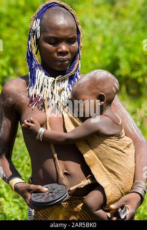 Mursi donna che allatta il suo bambino e vende piatti. Le donne Mursi sono famose di indossare piatti nelle loro labbra inferiori. Il motivo di questo 'ornamento' Foto Stock