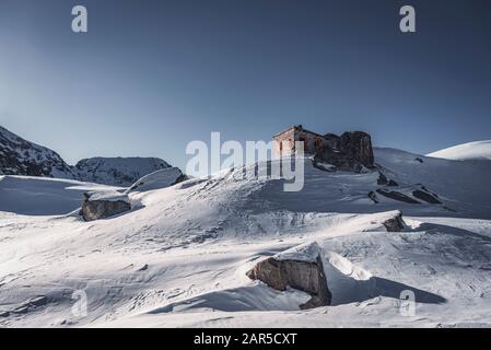 Ghiaccio e neve coperta piccola capanna di riparo di pietra, in piedi sulla cima della vetta in inverno Foto Stock