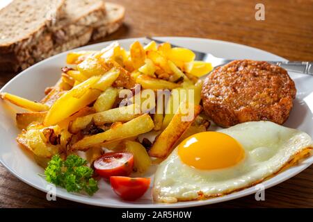Patatine fritte con uova fritte e un grande polpette sul piatto Foto Stock