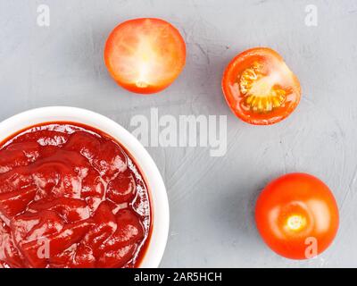 Pasta di pomodoro in una ciotola bianca e pomodori su fondo grigio in cemento. Concetto di alimentazione sana Foto Stock