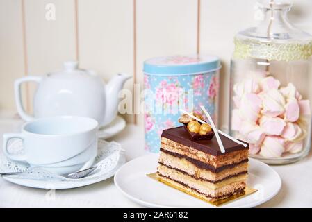 Una fetta di torta con noci e una teiera con una tazza sul tavolo. Foto Stock