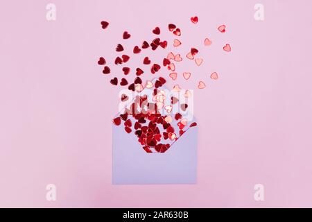 Piccoli cuori rossi lucenti con busta su sfondo rosa Foto Stock