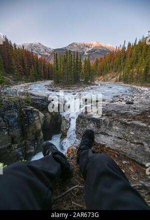 Il viaggiatore di gambe si siede allungando sulle Cascate Sunwapta in Icefields Parway al parco nazionale di Jasper, Canada Foto Stock