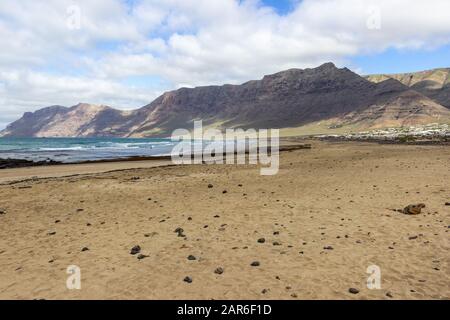 Costa e spiaggia di sabbia Playa de Famara con catena montuosa e onde oceaniche sull'isola delle canarie Lanzarote, Spagna Foto Stock