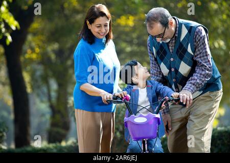 Nonni con nipote imparare a guidare la bicicletta Foto Stock