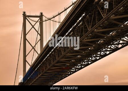 Forth Road Bridge (costruito nel 1964) dal basso con cielo arancione. Questo ponte è ora utilizzato solo per i trasporti pubblici che seguono la costruzione di un nuovo ponte. Foto Stock