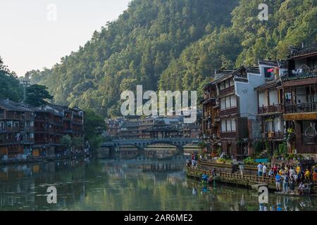 Feng Huang, Cina - Agosto 2019 : Persone che camminano su un sentiero stretto lungo le vecchie case storiche di legno di palafitta Diaojiao sulle rive del fiume Tuo, Foto Stock